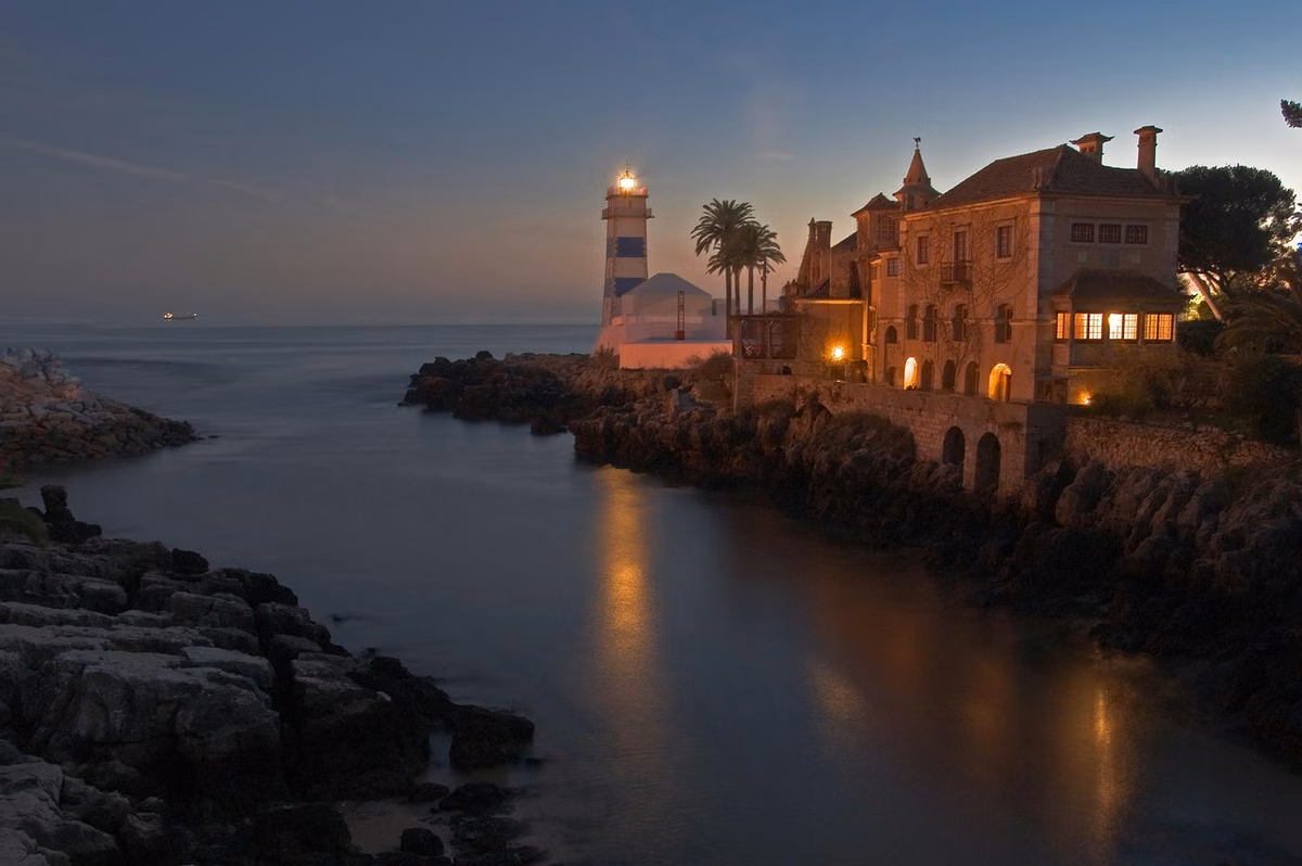 Cascais at dusk, the lighthouse and the waterfront mansion lit above the rocks