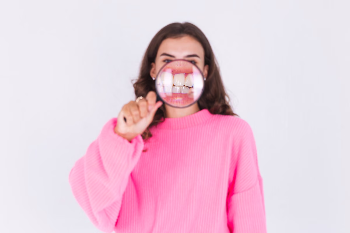 Woman in a pink jumper looking through a magnifying glass that enlarges her mouth