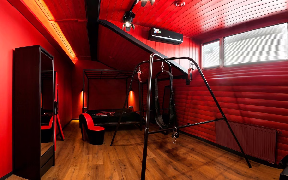 A red-lit room with bondage suspension equipment and a wooden floor