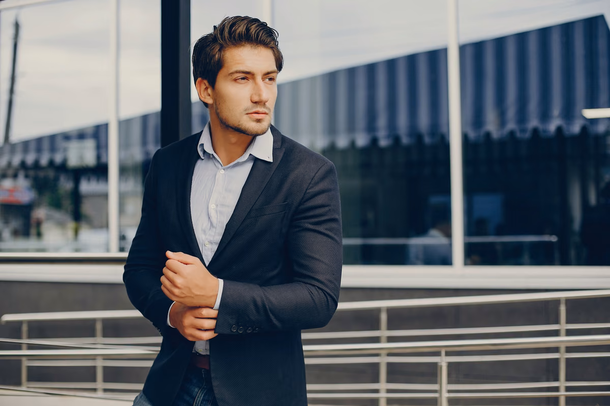 Man in a suit standing on a balcony, a glass building behind him